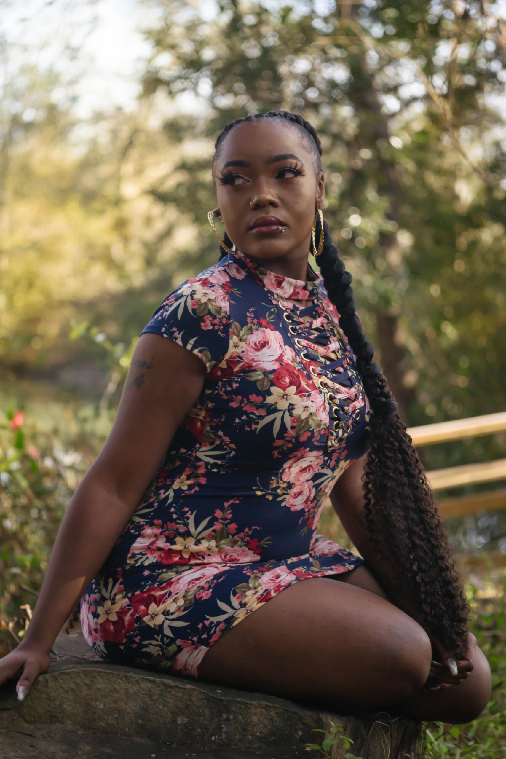 Beautiful woman in a floral dress posing outdoors in a summer park setting.